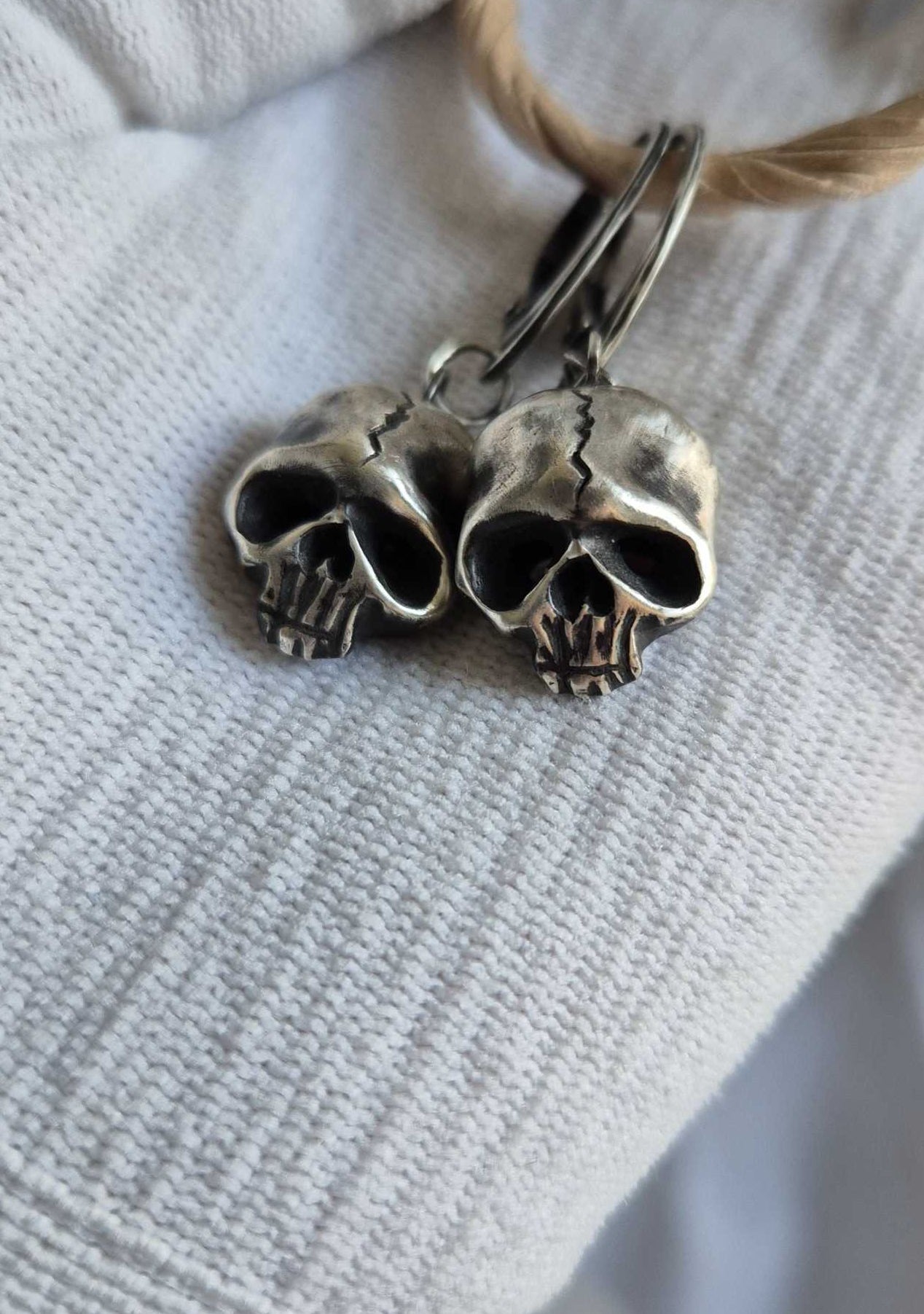 Close view of silver Skull earrings showing their expressive, miniature anatomy, in gloved hand