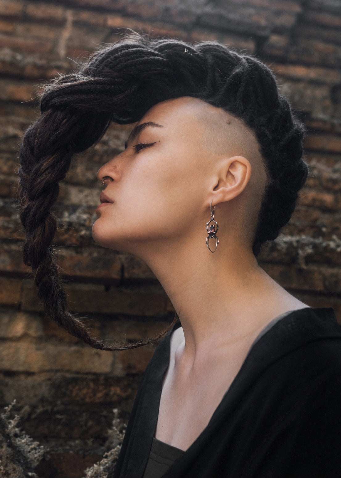 Handmade oxidized silver spider earrings with natural red garnets, worn by a model dreadlocks with shamanic vibe on textural background