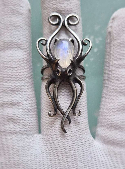 Silver octopus ring with moonstone shown on a white-gloved hand against teal background