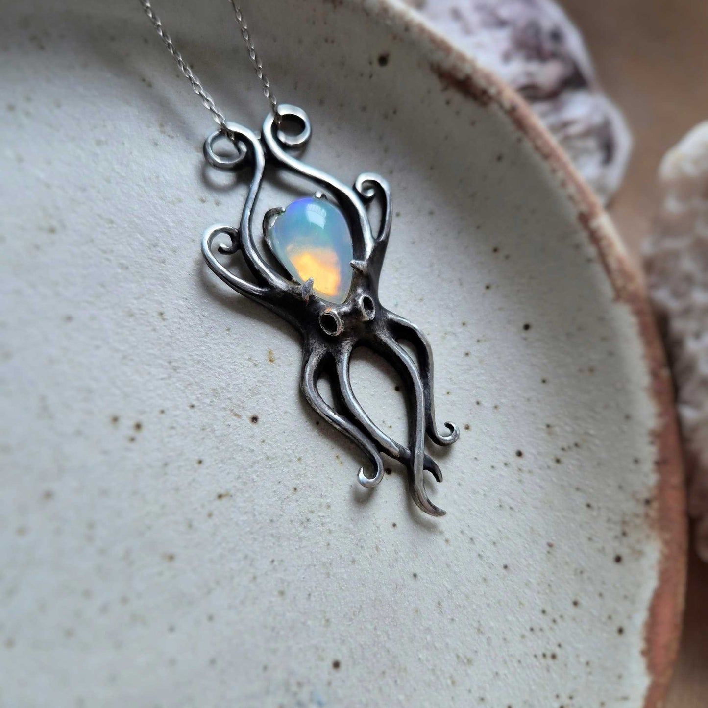 Sterling silver Octopus necklace with opal gemstone, elegant tentacle design, photographed on a rustic dish.