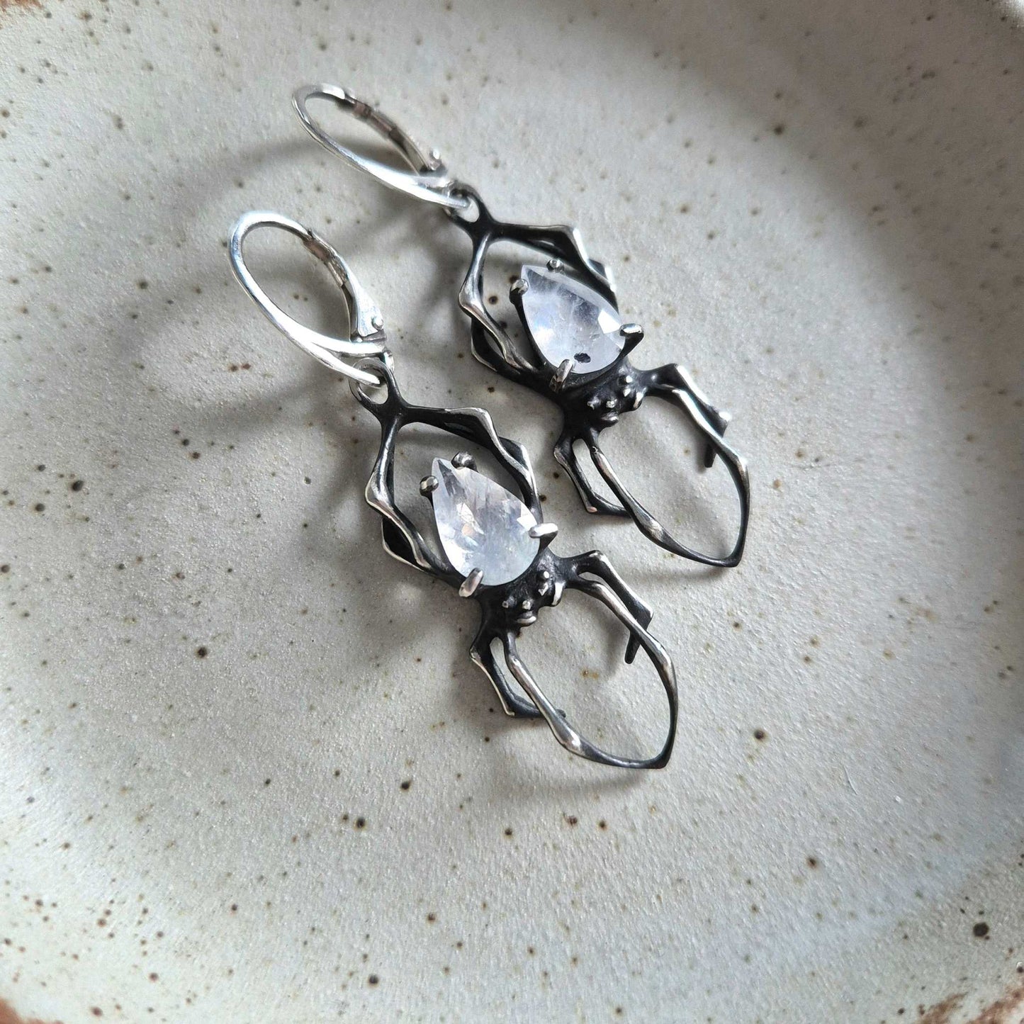 Close-up of silver Spider earrings with rainbow moonstones on white background