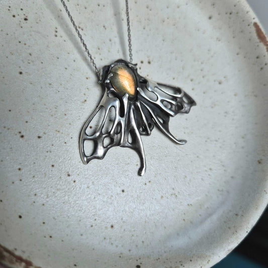 Silver Moth necklace with golden labradorite gemstone on ceramic plate
