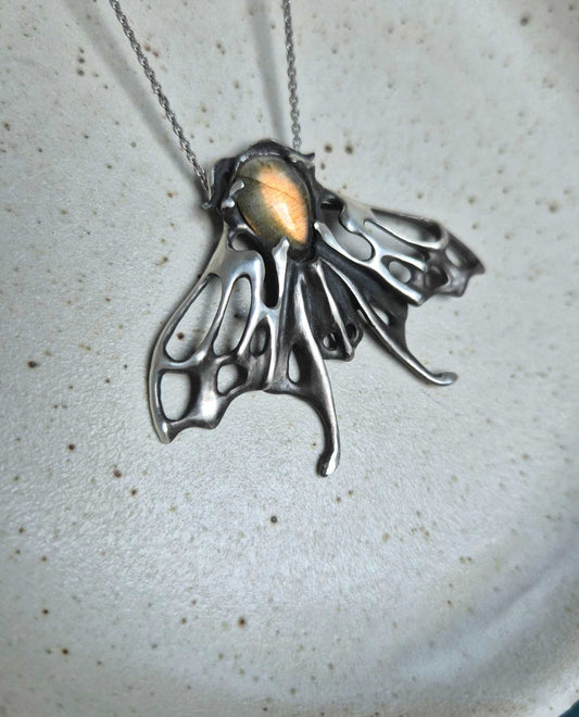 Silver Moth necklace with golden labradorite gemstone on ceramic plate