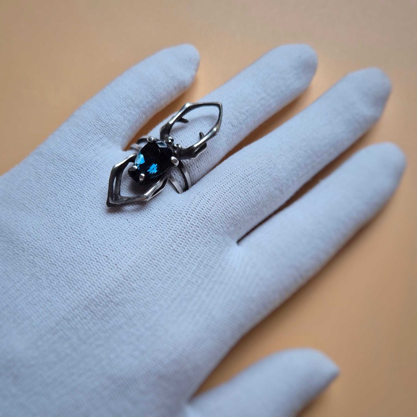 Close-up of silver spider ring with faceted London blue topaz, displayed on white gloved hand