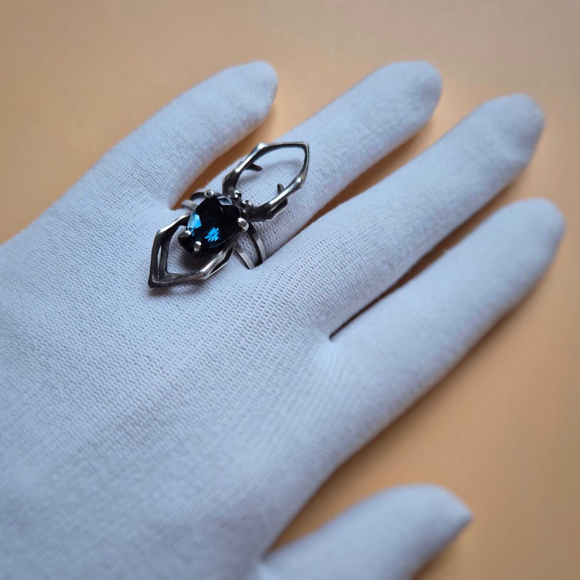 Close-up of silver spider ring with faceted London blue topaz, displayed on white gloved hand