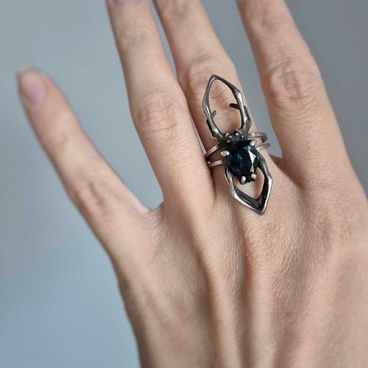 Hand wearing silver spider ring with London blue topaz gemstone, natural lighting