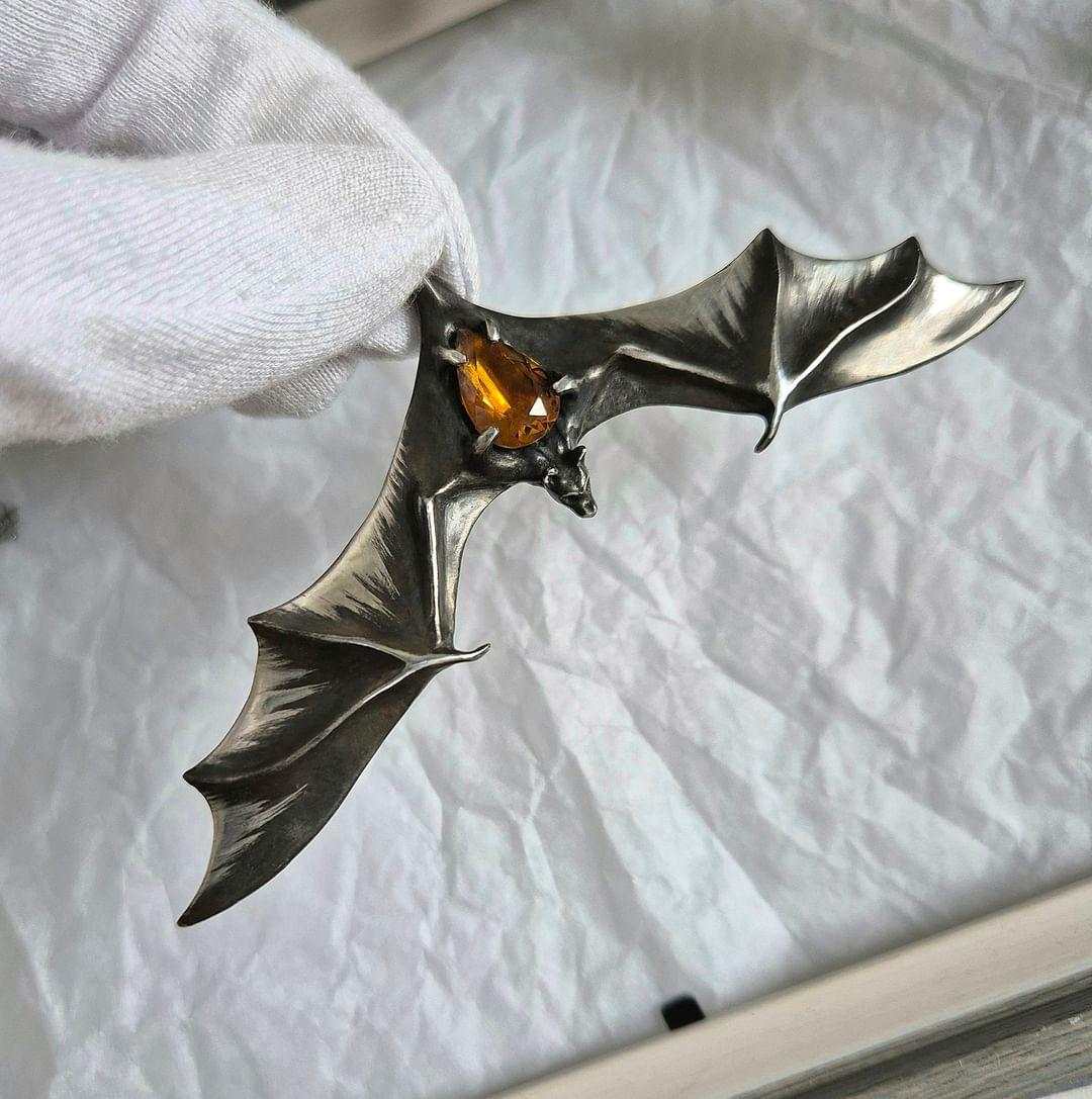 Hand holding silver Bat necklace with glowing yellow citrine set in the center