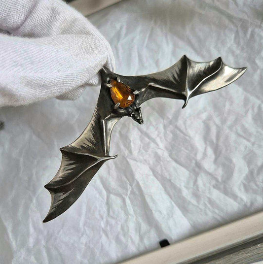 Hand holding silver Bat necklace with glowing yellow citrine set in the center