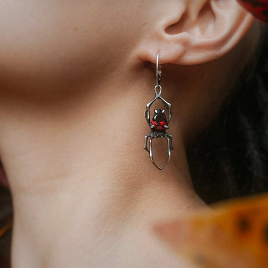 Close-up of handmade oxidised silver spider earrings with natural garnets, worn by a model in natural boho style