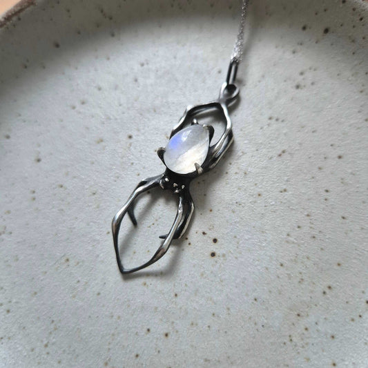 Silver spider necklace with pear-shaped rainbow moonstone on specled ceramic background