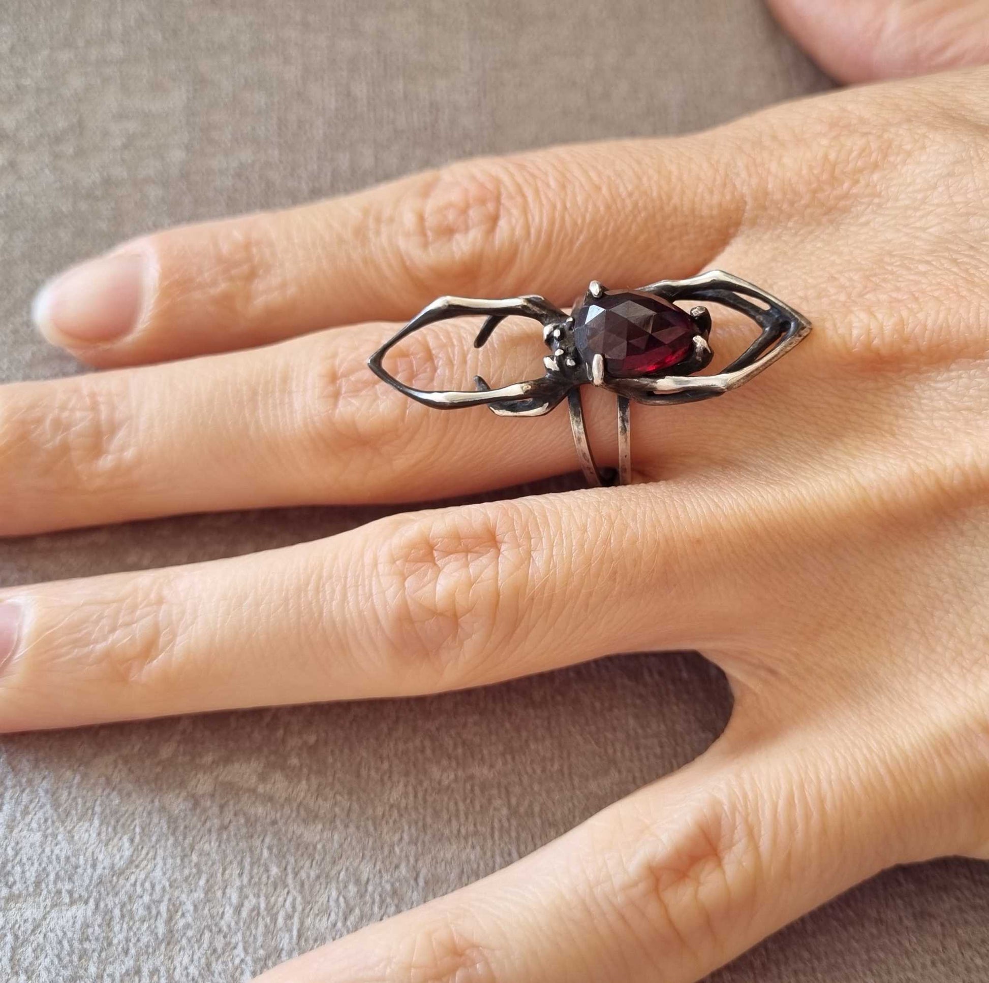 Side view silver of a Spider ring on hand, showing the intricate garnet centerpiece and sculptural design