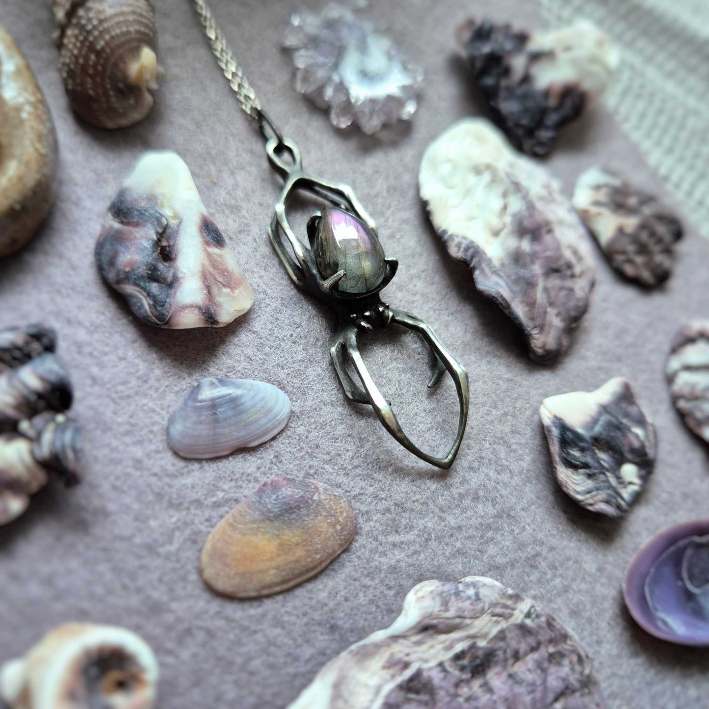 Silver Spider talisman with natural purple labradorite, displayed among seashells