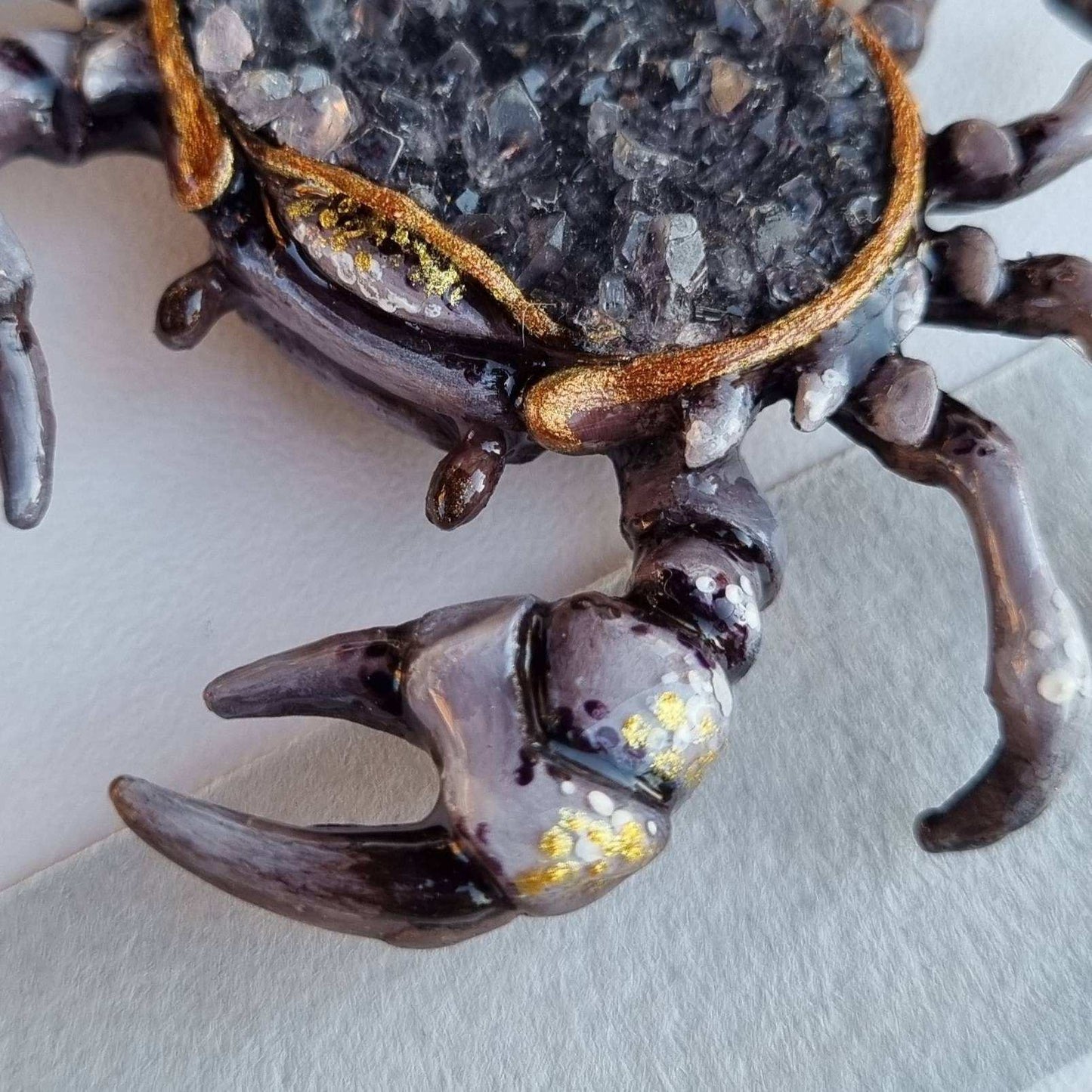 Side angle of crab figurine with dark quartz crystals, claws in focus.