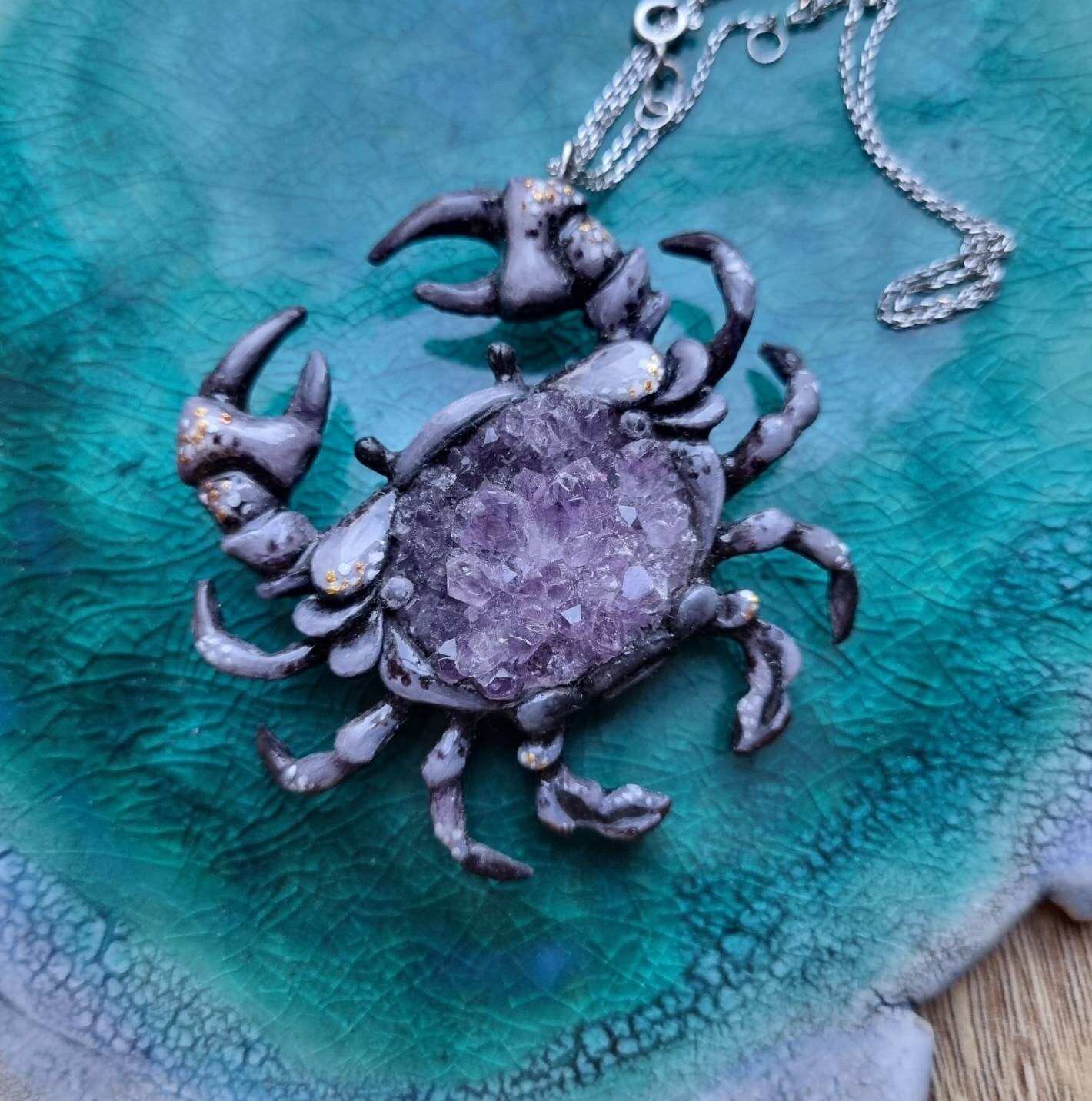 Crab necklace with amethyst druzy center, displayed on teal ceramic surface