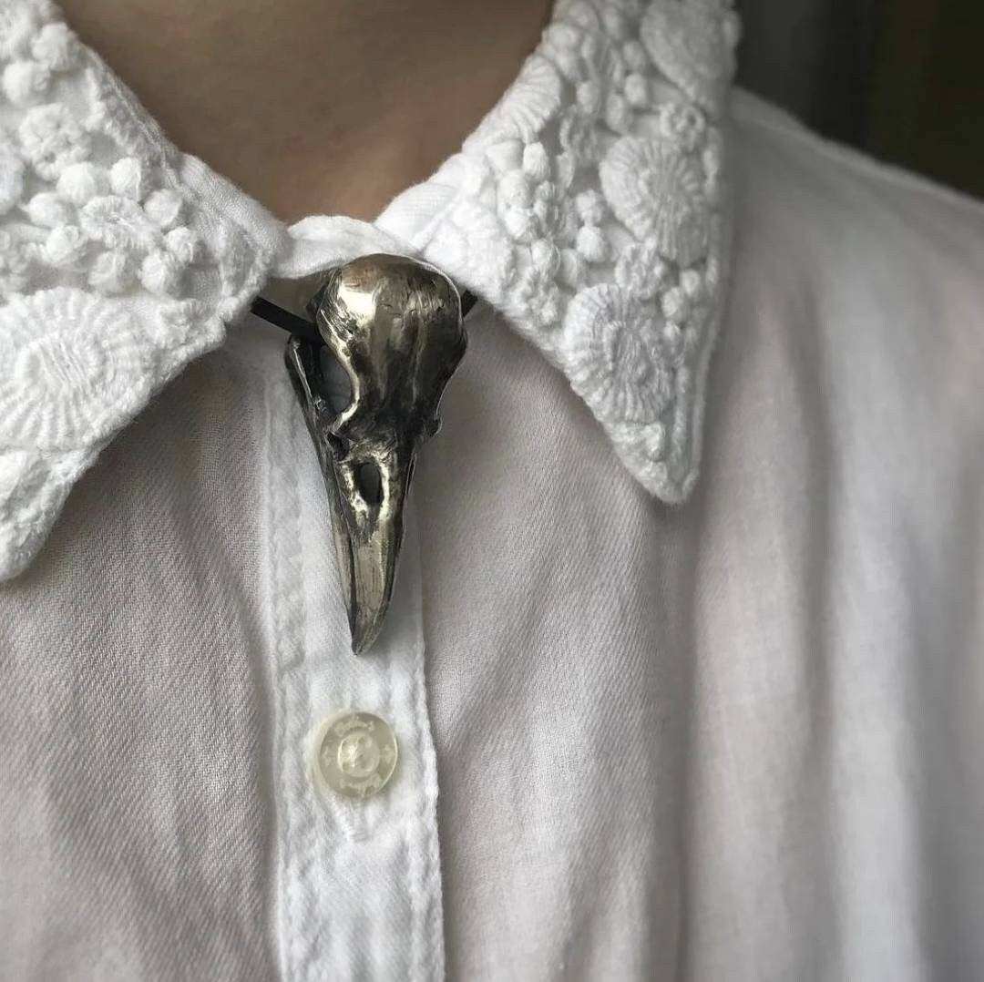 Raven skull pendant styled under a shirt collar as a gothic accent.