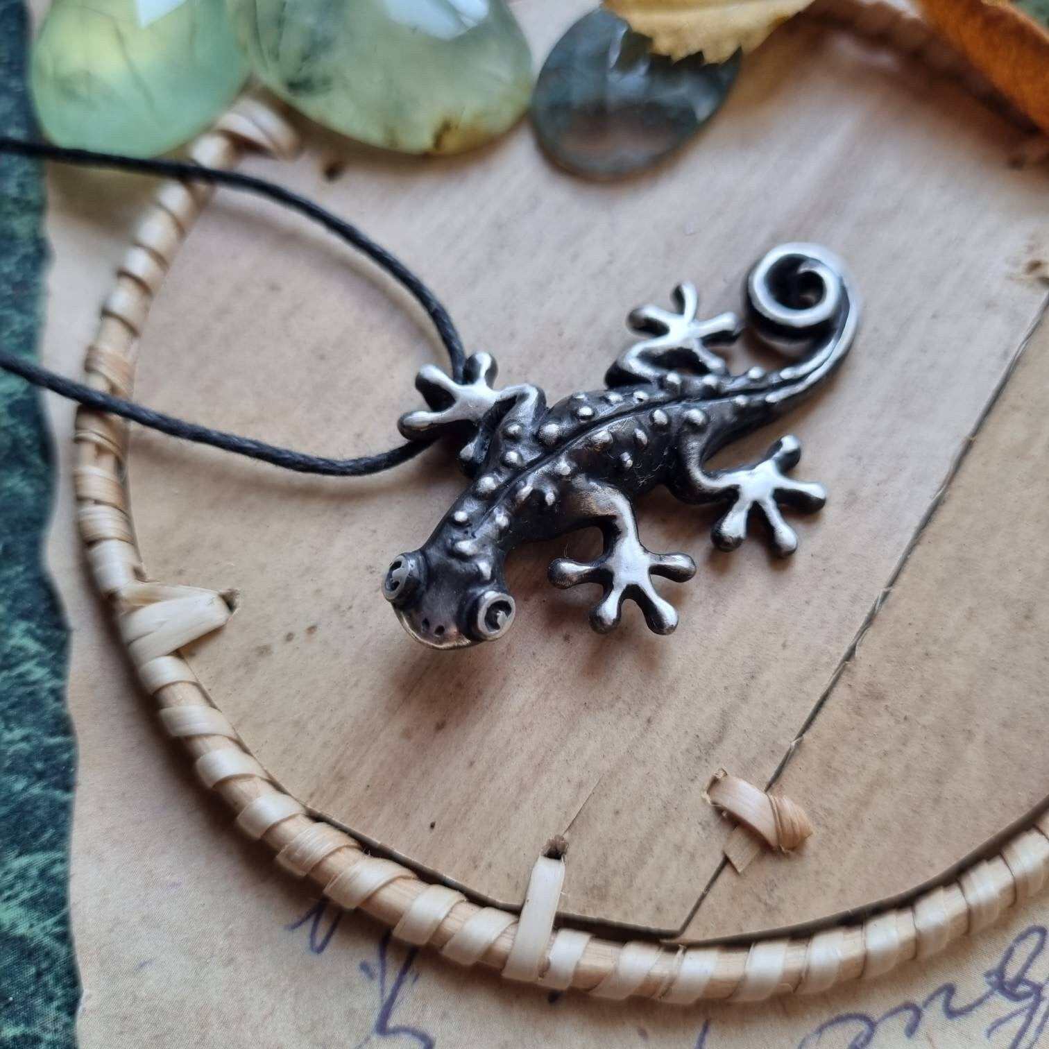 Silver gecko pendant displayed on a warm-toned surface with decorative props