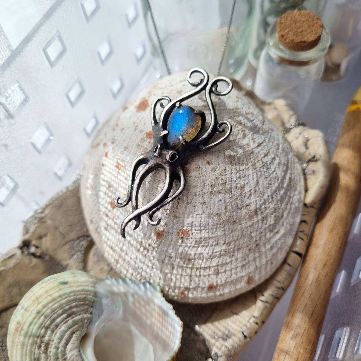 Handcrafted silver Octopus pendant with blue labradorite, resting on rustic glass and natural textures.