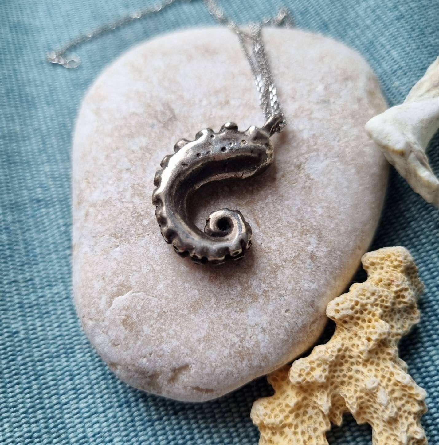 Tentacle necklace close-up on a pale stone and coral, softly lit.