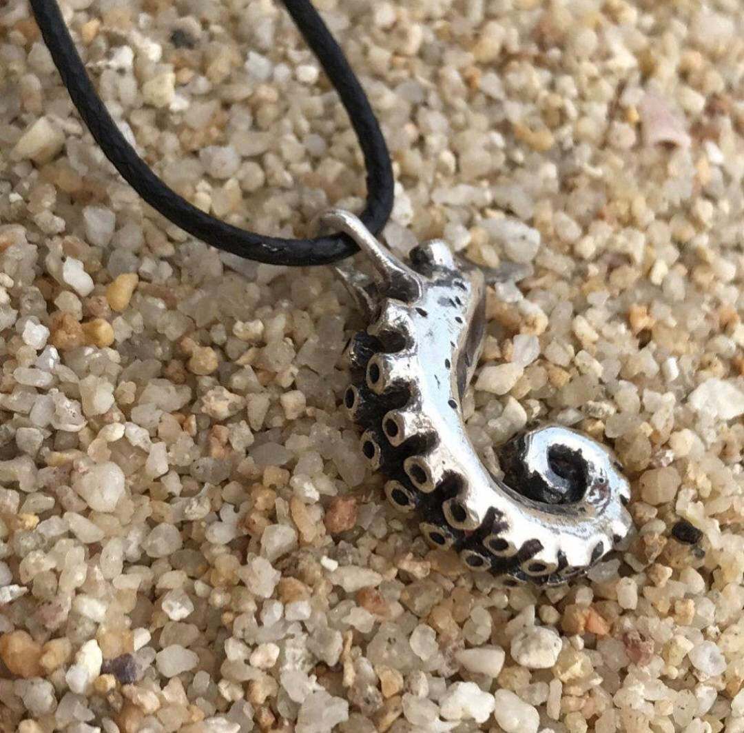 Tentacle pendant on dark cord, lying on sand with delicate shadows.