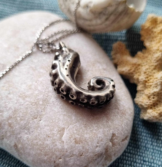 Silver octopus necklace displayed on a smooth stone with coral.