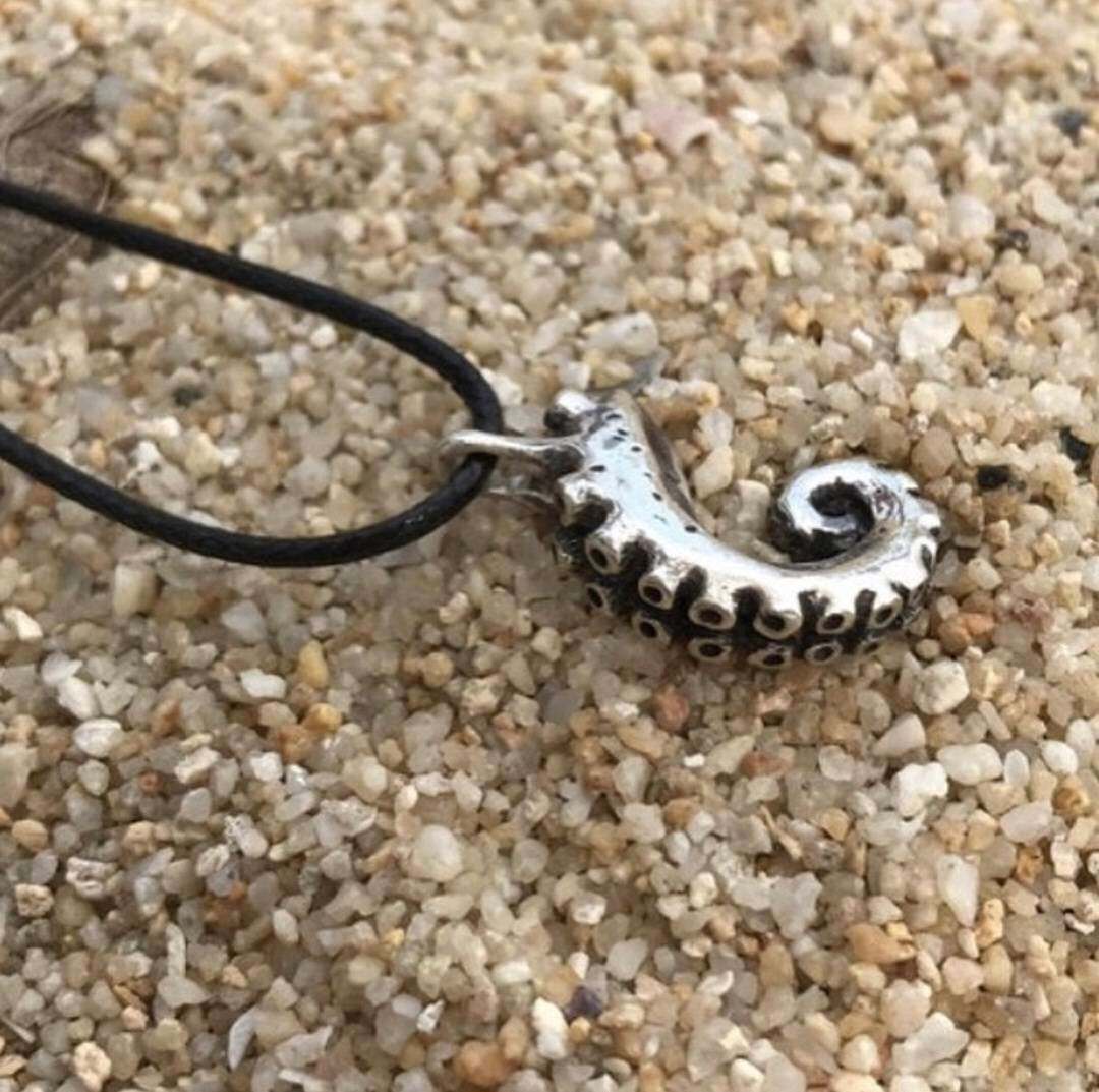 Tentacle necklace resting on sandy beach with cord looped above.