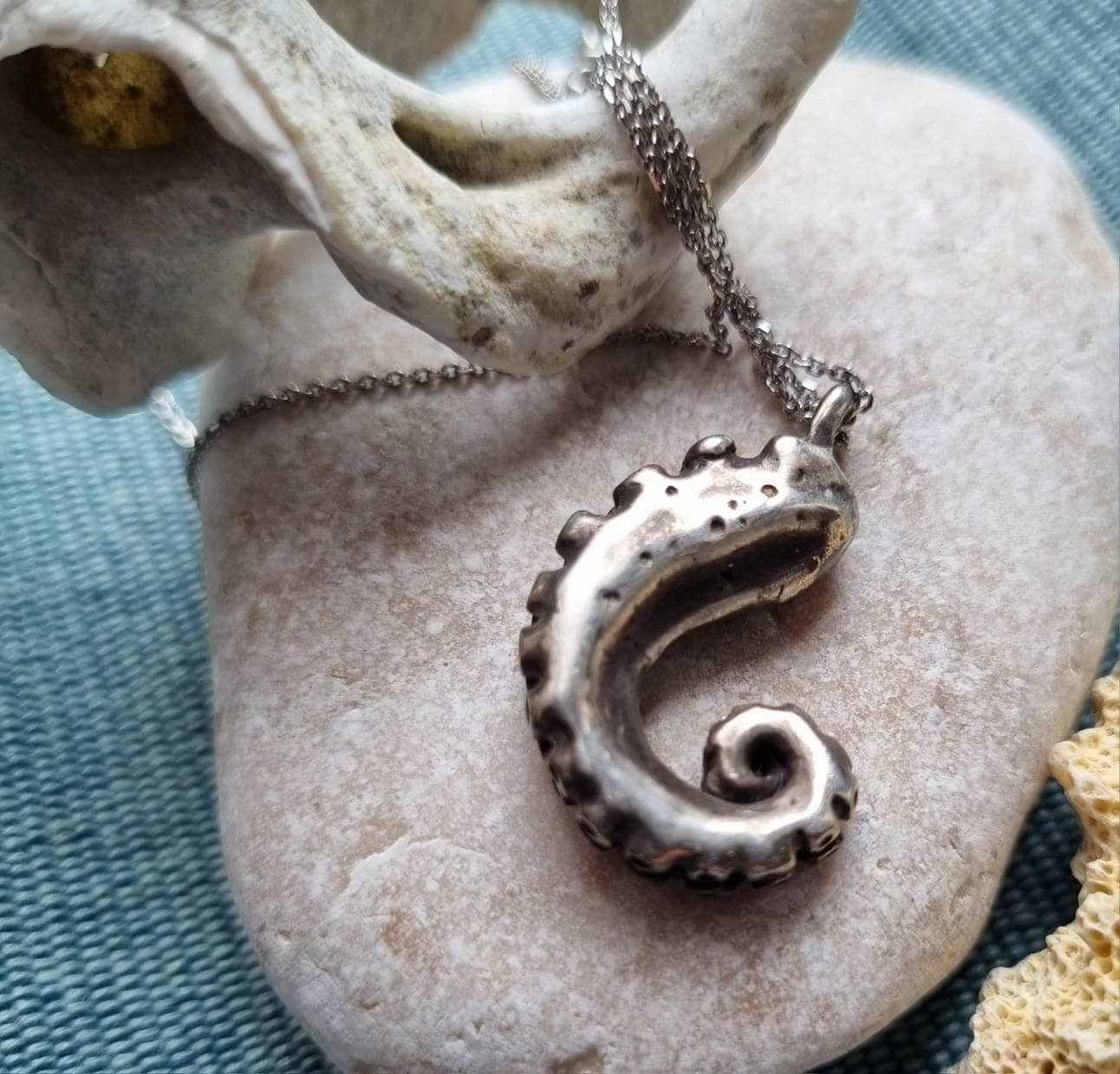 Silver tentacle pendant placed on pale stone with beige coral.