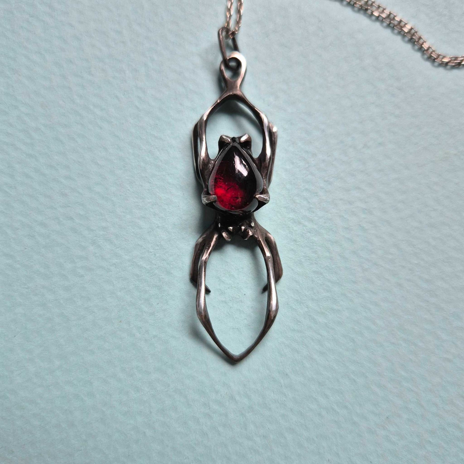 Close-up of silver spider pendant with deep red garnet – gothic spider necklace