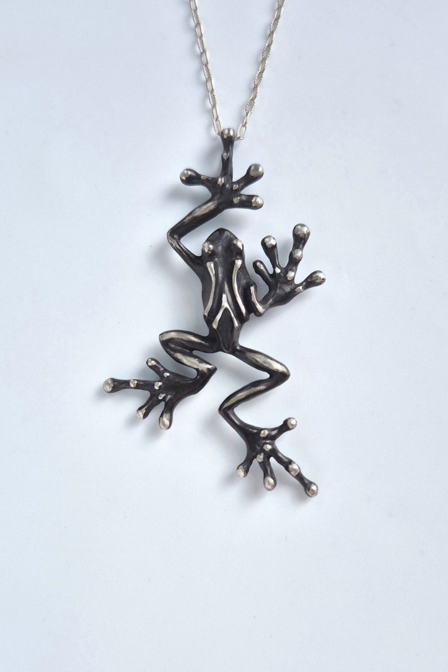 Front view of a leaping sterling silver frog necklace with chain on a white background