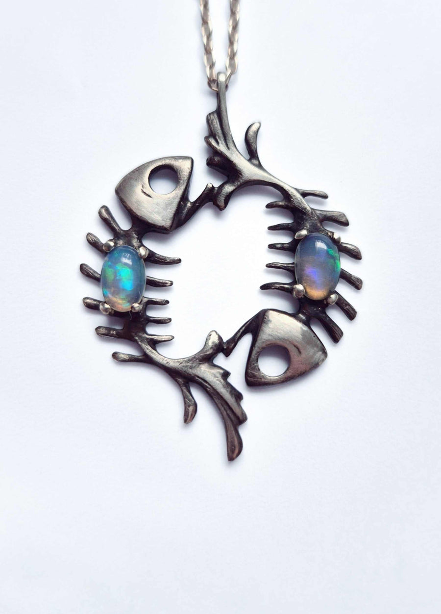 Close-up of oxidized sterling silver fish skeleton necklace with two Ethiopian opals on a white background