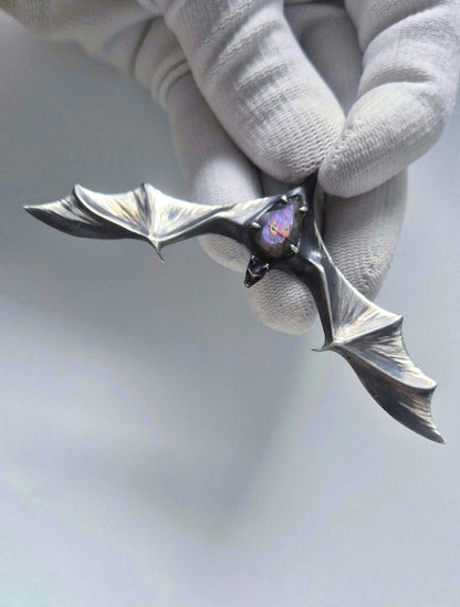Oxidized silver bat pendant with purple-flash labradorite held by its bail in a white-gloved hand