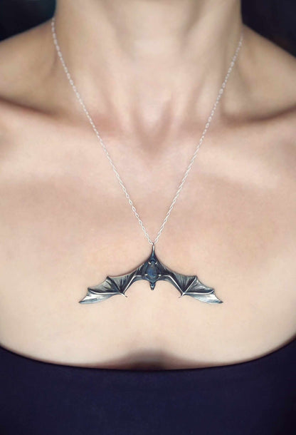 Wide sterling silver bat necklace with dark blue gemstone worn at the center of the chest