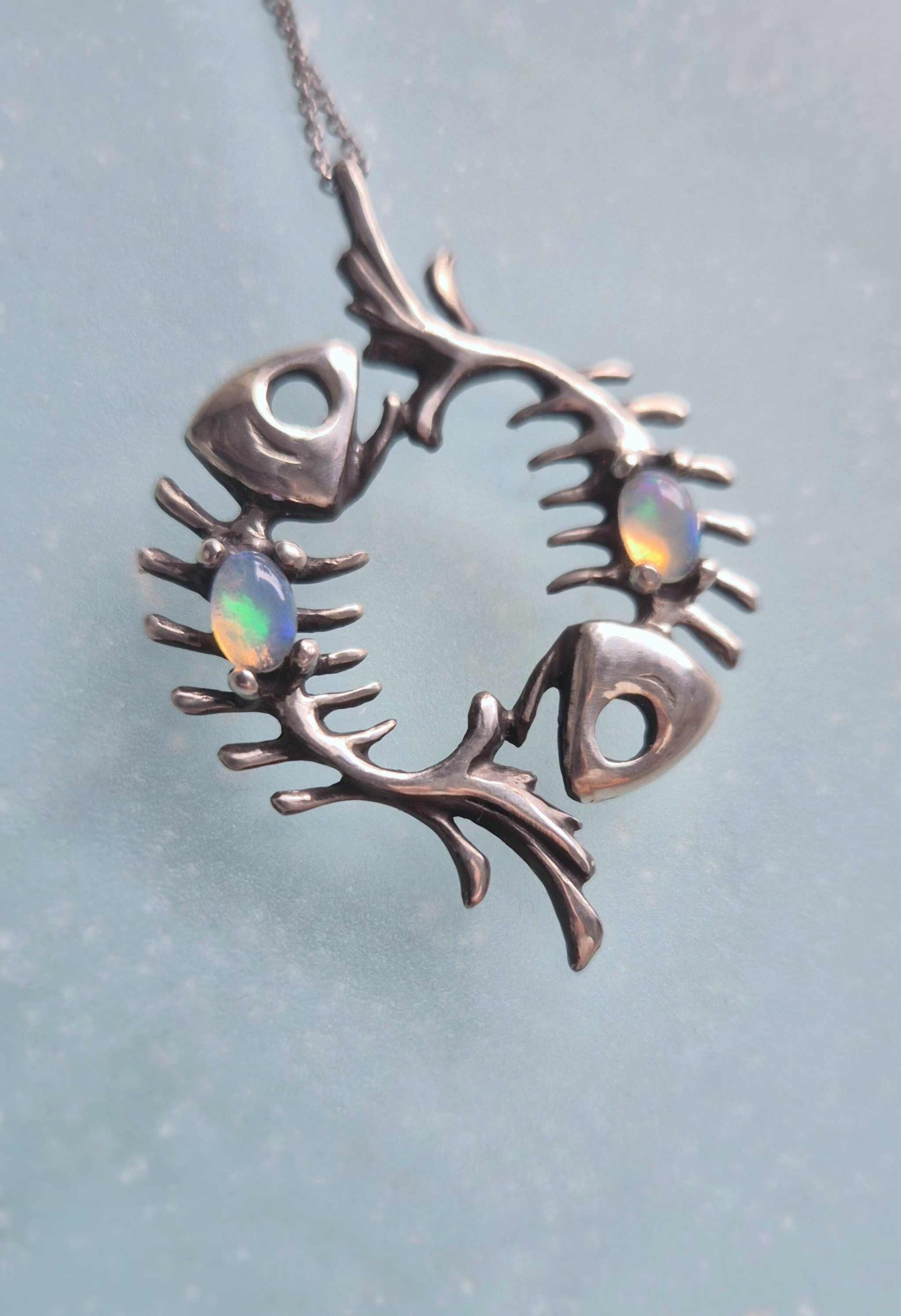 Macro view of two Ethiopian opals set in an oxidized silver fish skeleton pendant on pale blue