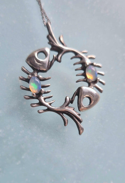 Macro view of two Ethiopian opals set in an oxidized silver fish skeleton pendant on pale blue