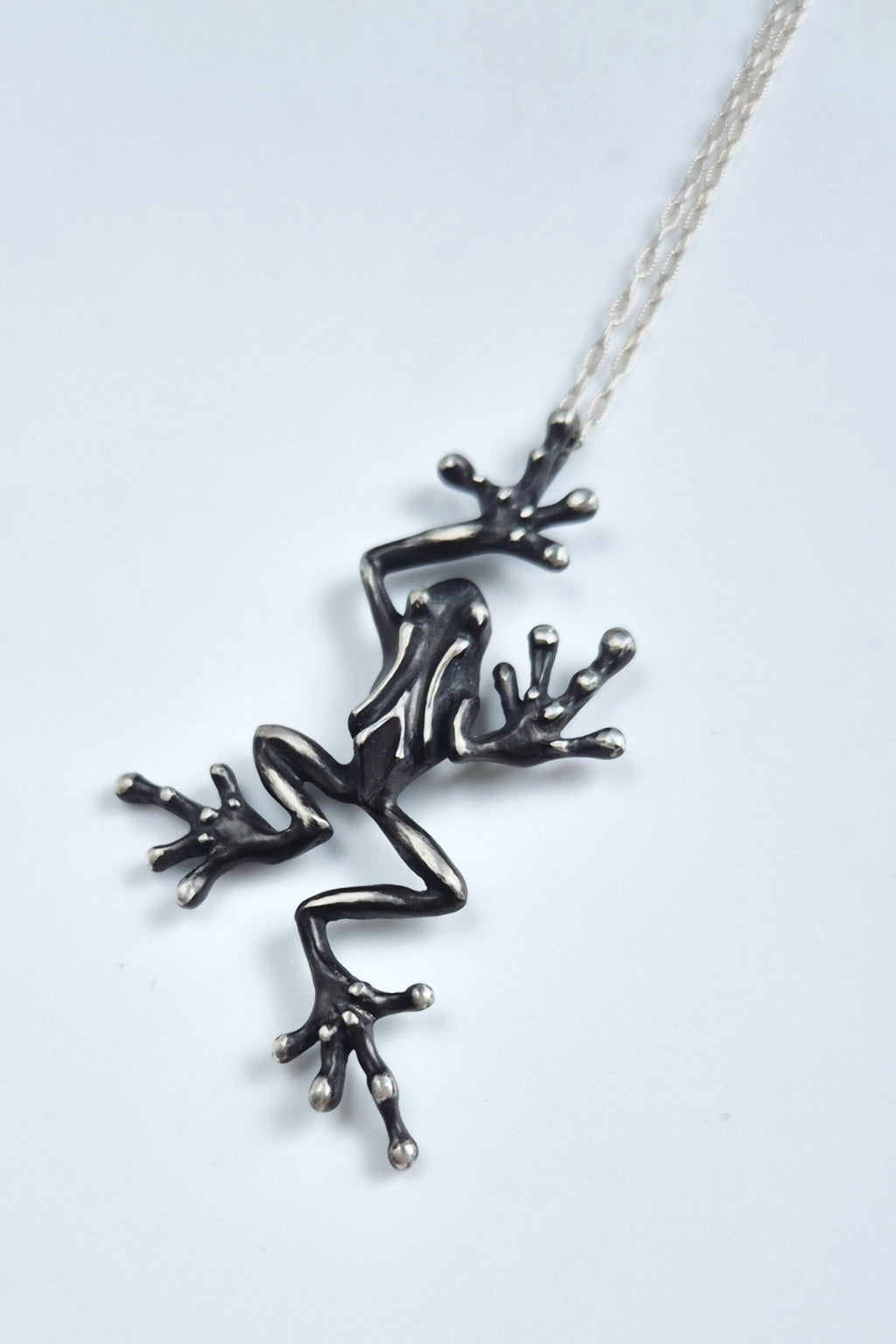 Full view of a leaping sterling silver frog pendant and chain on white