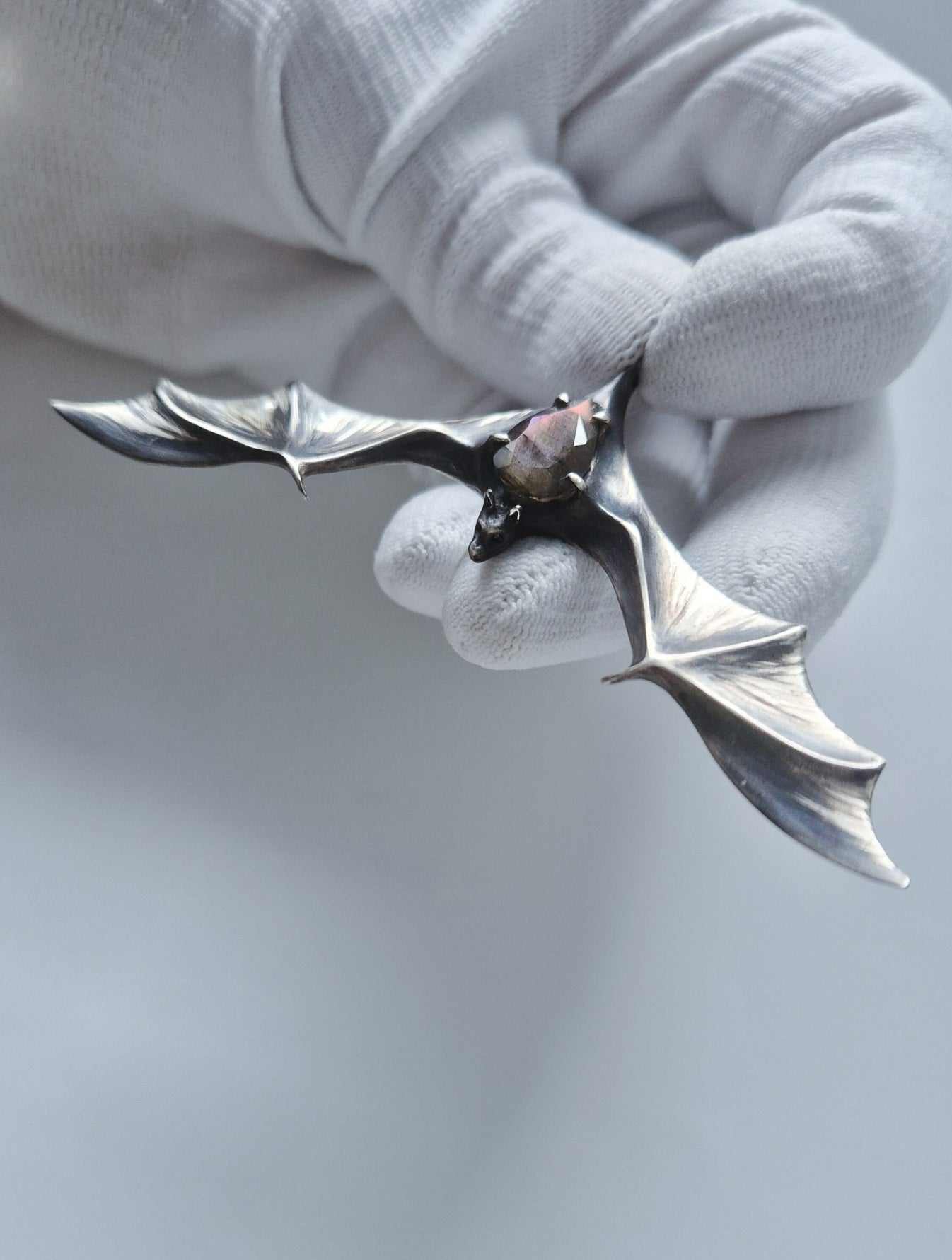 Angled silver bat necklace with multicolor labradorite held against pale gray