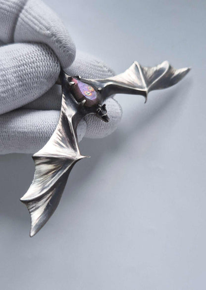 Close-up of the silver bat pendant and purple-patterned labradorite held in a white glove