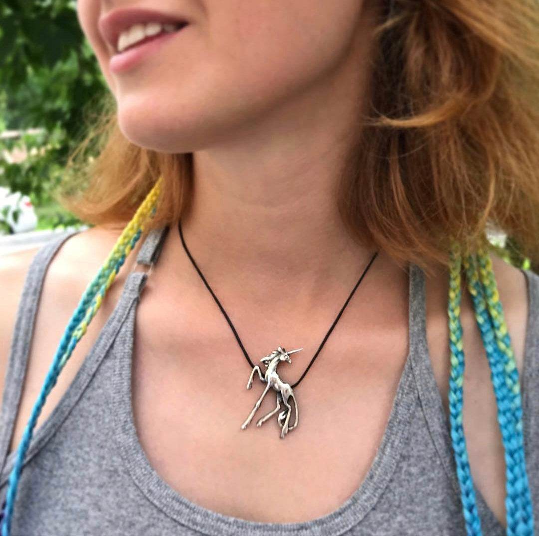 A person wearing the silver Unicorn necklace on a cord, with the pendant centered below the collarbone.