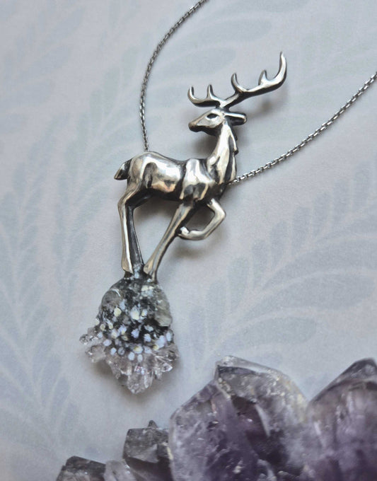 Silver deer necklace with rough-textured body and raw quartz crystal, displayed on amethyst and patterned background