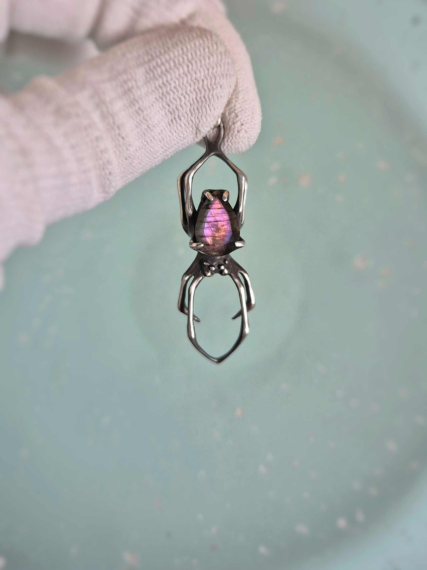 Silver spider necklace with purple labradorite, held against a pale blue background.
