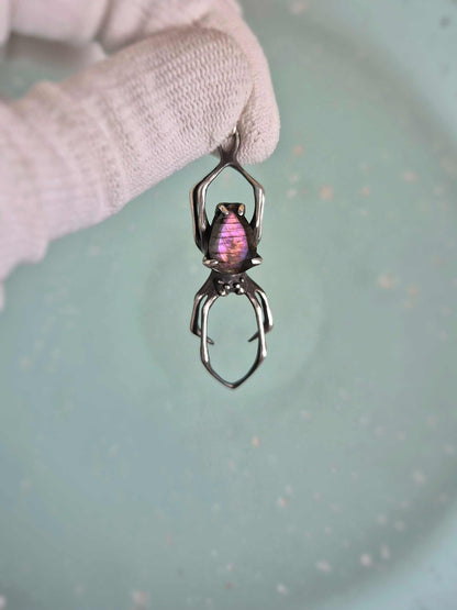 Silver spider necklace with purple labradorite, held against a pale blue background.