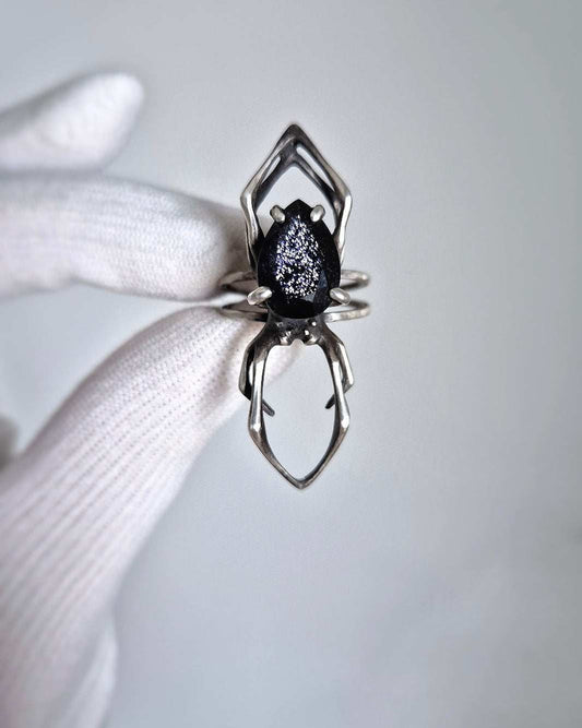 Silver spider ring with iolite sunstone held in gloved hand, shown close-up against soft light background