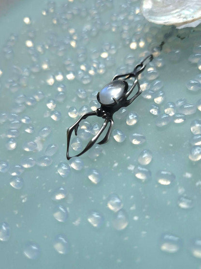 Spider-shaped silver necklace with glowing moonstone on textured pastel surface