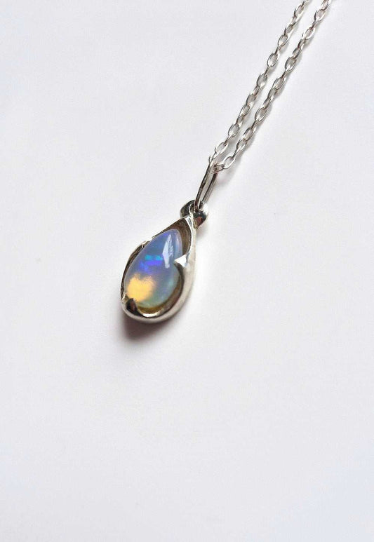 Sterling silver opal pendant with teardrop shape, iridescent blue fire, photographed against a white background