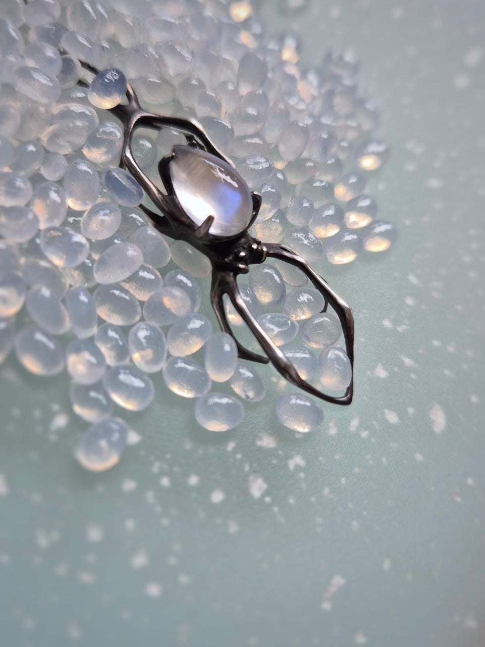 Silver spider necklace with moonstone on light blue background with scattered beads