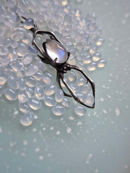 Silver spider necklace with moonstone on light blue background with scattered beads