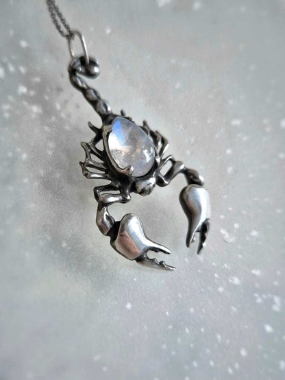 Silver Scorpion necklace featuring rainbow moonstone, photographed against soft grey marble background.