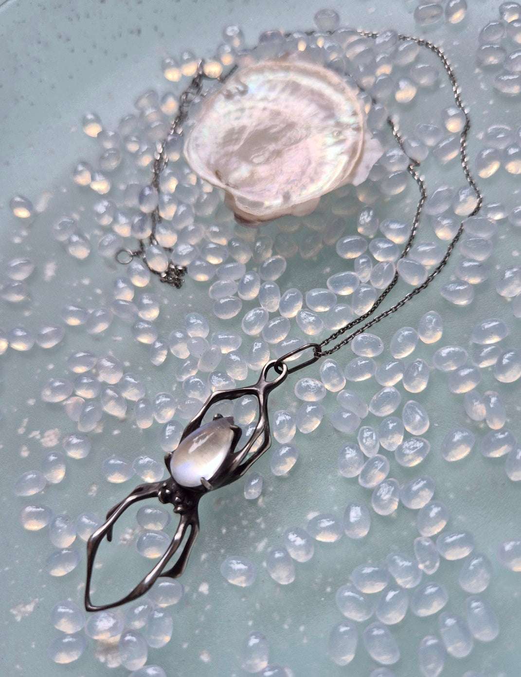 Close-up of moonstone spider pendant lying near soft shell on beaded background