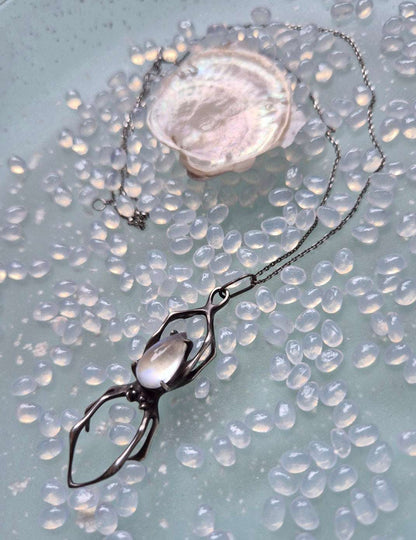 Close-up of moonstone spider pendant lying near soft shell on beaded background