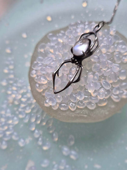 Artistic composition of silver spider necklace with moonstone and shell accent