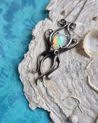 Handmade silver octopus pendant featuring an iridescent opal, photographed on a seashell surface